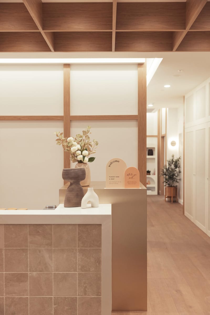 A modern reception desk with minimalist decor, including a vase of flowers and geometric sculptures, in a softly lit interior with wood accents.